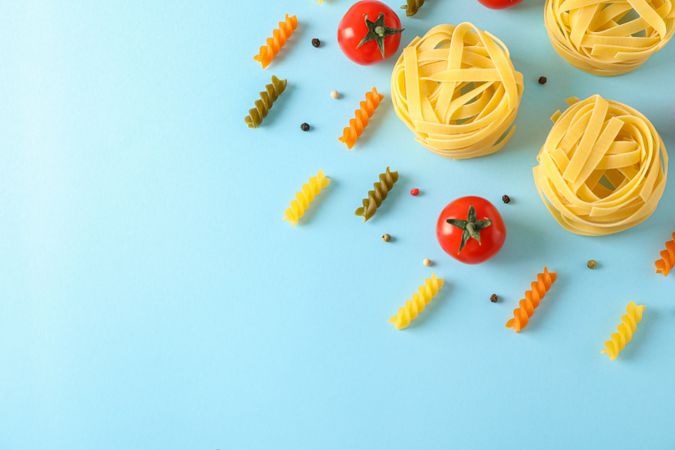 Flat lay composition with different pasta and tomatoes on color background, space for text. Dry uncooked whole pasta