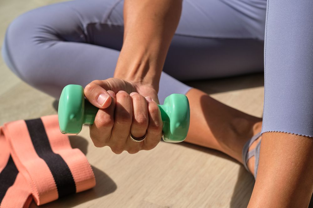 Female sitting on floor with dumbbell in hand during workout in sunlight