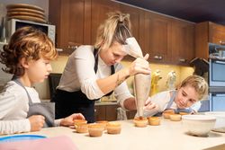 Mother and children decorating cupcakes with cream in kitchen