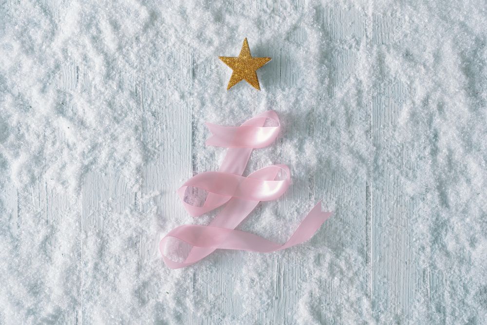 Wooden table background with snow and festive pink ribbon tree decoration