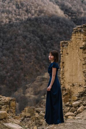 Side view of mature woman in long blue dress standing in natural landscape