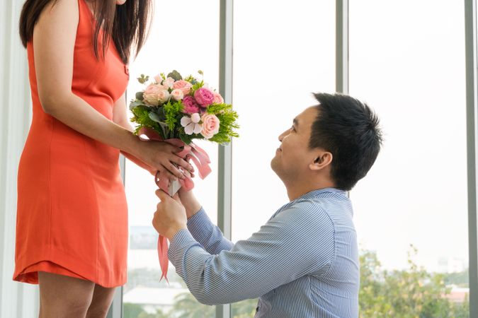Asian male down on one knee with flowers proposing to girlfriend
