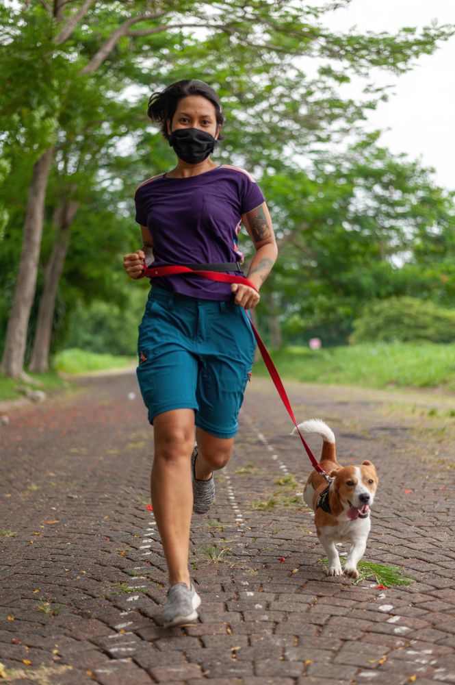 Woman with facemask running with her dog in the park