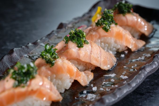 Appetizing nigiri sushi with salmon slices garnished with fresh herbs and salt served on marble plate