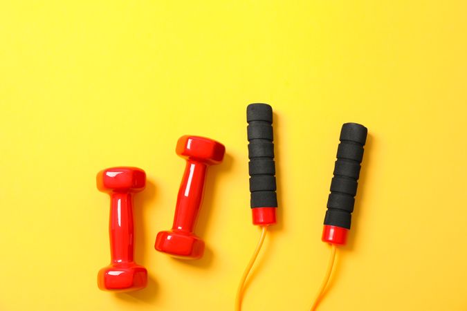 Dumbbells and jump rope on yellow background, space for text