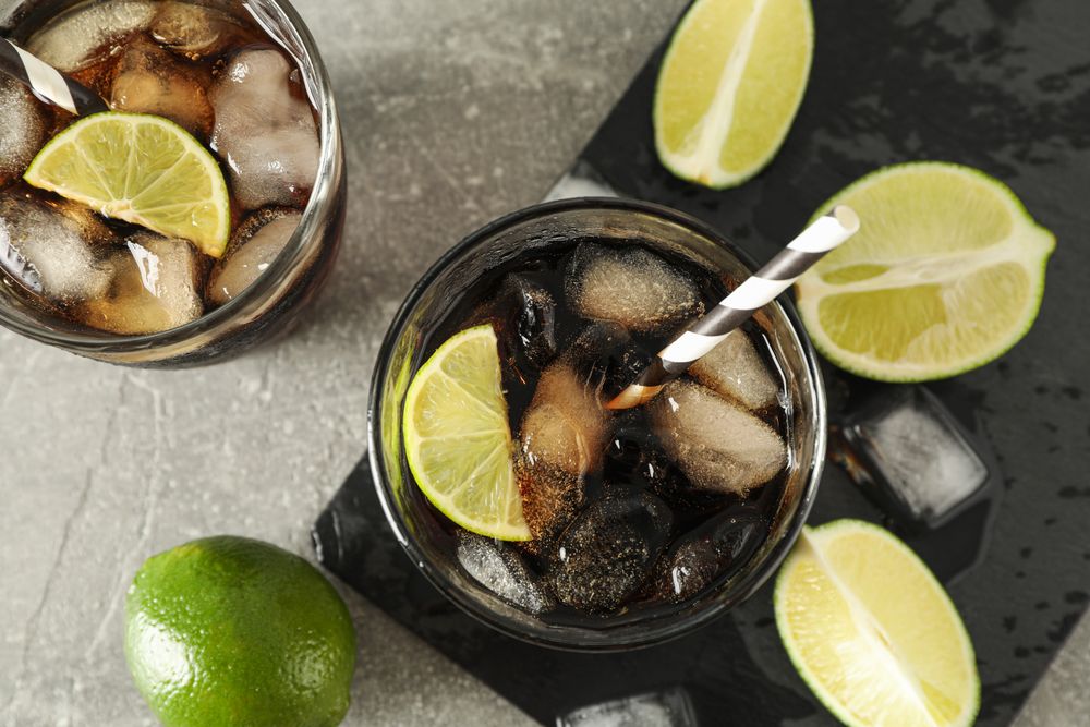 Glasses with cold cola and citrus on grey table, top view