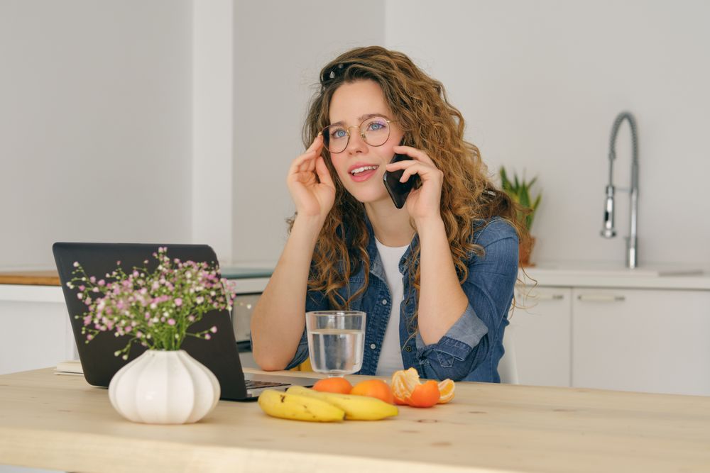 Thoughtful woman talking on smartphone in kitchen