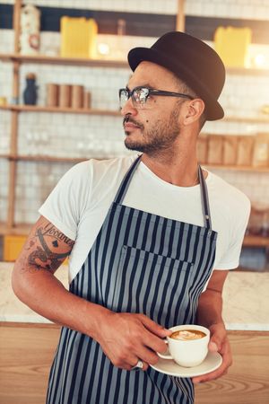 Portrait of young man working in coffee shop standing at bar counter and looking away