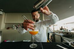Barman pouring cocktail and alcoholic drinks from shaker in a bar.
