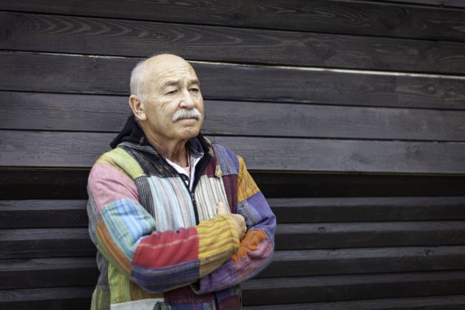 Pensive mature man with arms folded against house