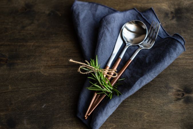Cutlery set on navy napkin on wooden table with rosemary garnish