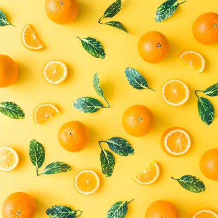 Oranges and green leaves on pastel yellow background