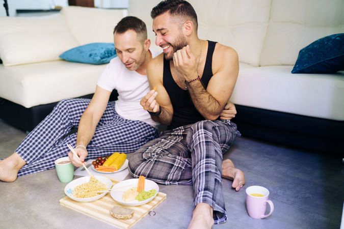 Content male couple enjoying relaxing meal at home sitting on floor