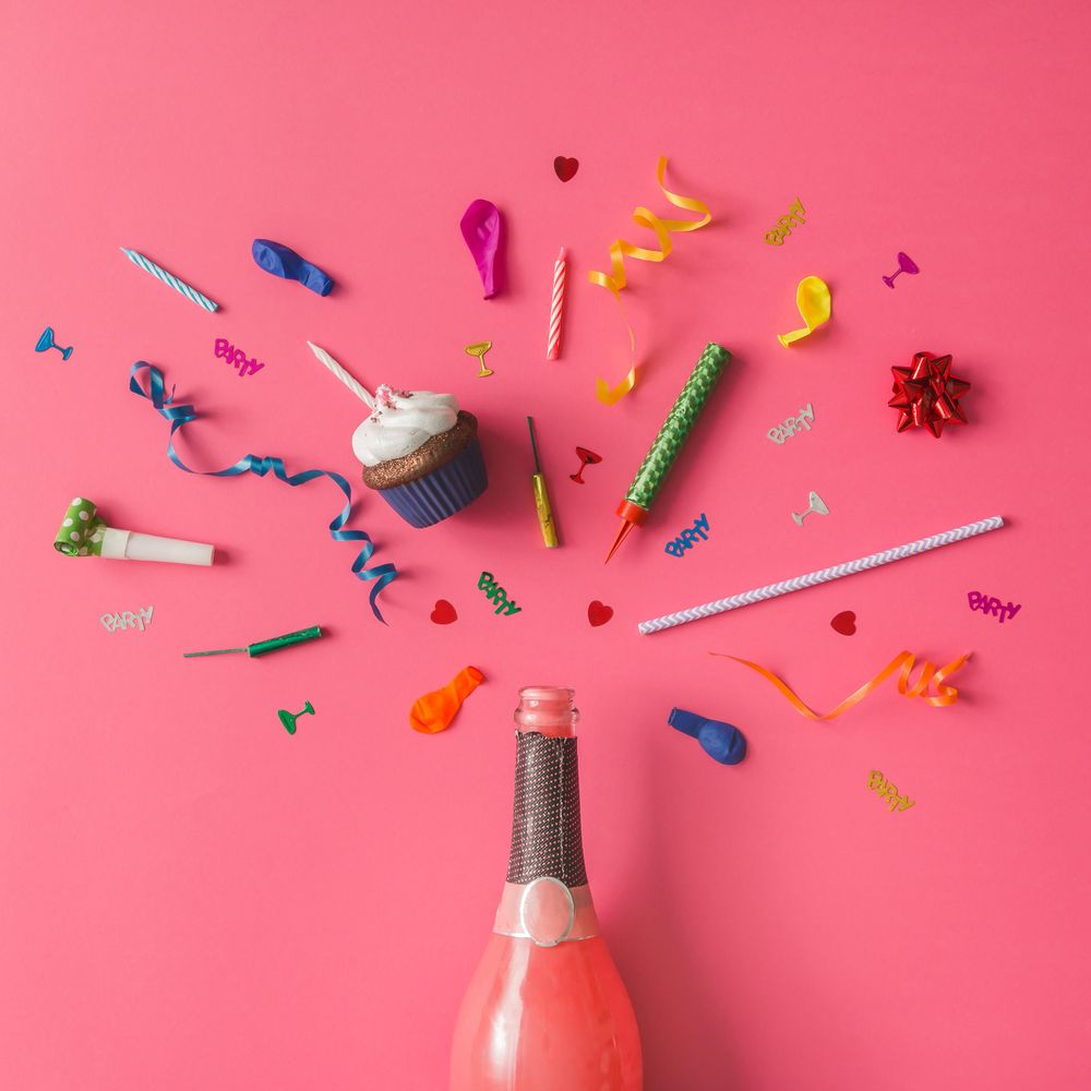 Champagne bottle with colorful party items on pink background