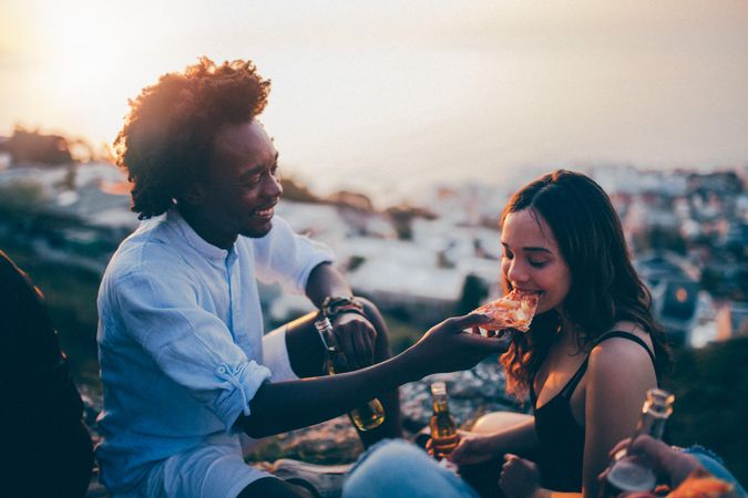 A man feeds a woman a slide of pizza outdoors