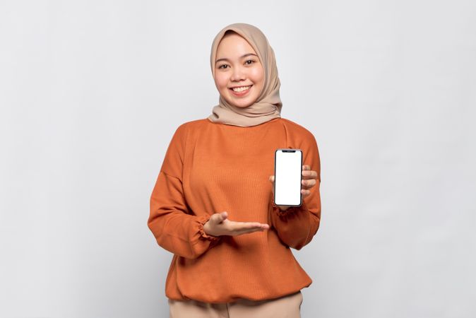 Happy Muslim woman smiling presenting smart phone with mock up screen