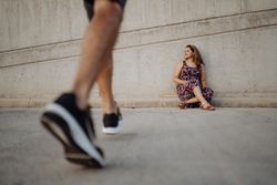 woman sitting on grey wall while crop man is walking to her