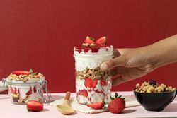 Hand reaching for very parfait with layered granola, fruit and yogurt