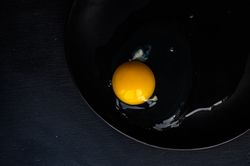 Cracked raw egg on dark surface