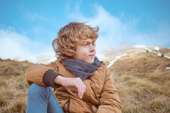 Boy sitting on hillside against blue sky and steam