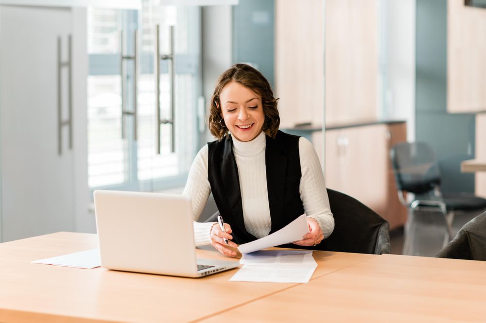 Smiling woman sitting at a table in the office working on her laptop