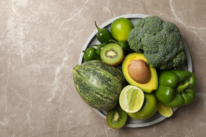 Tray with green fruits and vegetables on gray table