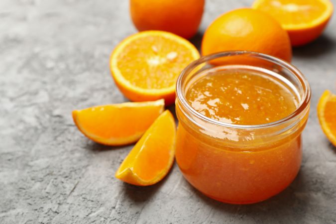 Oranges and glass jar with jam on gray background, close up