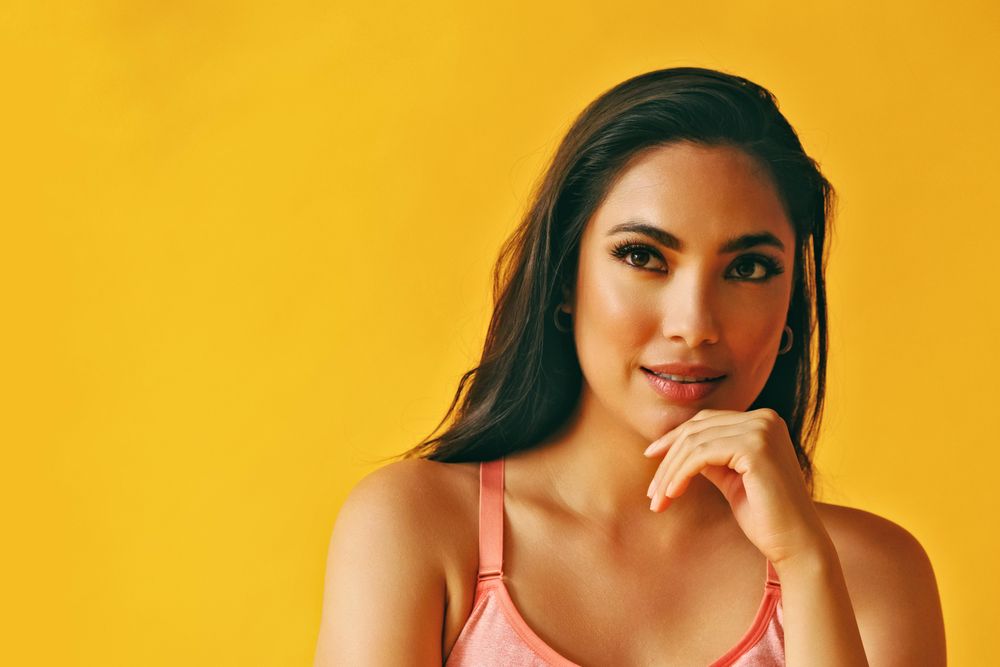 Headshot of Hispanic woman deep in thought in front of a yellow background