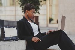 Stylish Black woman with laptop on steps near handbag