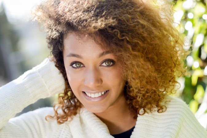 Woman with curly hair standing outside looking at camera and touching hair