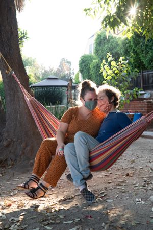 Wife and husband snuggle close while sitting in a hammock