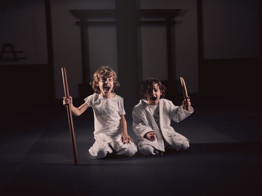 Funny kids in judogi sitting on mat with wooden sticks and shouting