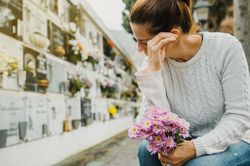 Woman with flowers crying near columbarium wall in cemetery