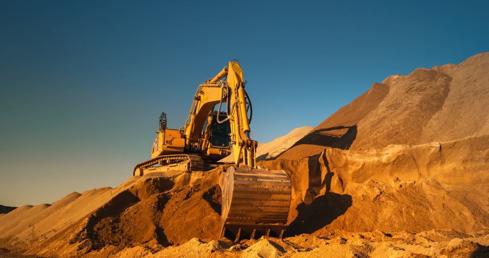 Construction Site On A Hot Sunny Day: Industrial Excavator Digging Sand To Lay Foundation for Building New Apartment Block. Workers Operating Heavy Machinery To Complete A Real Estate Project.