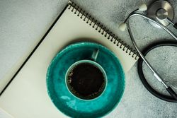 Coffee in teal cup with phone, stethoscope and notepad