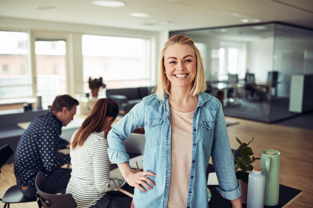Portrait of blonde business woman smiling in an office with hand on hip