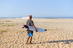 Unrecognizable man with surfboard walking on beach