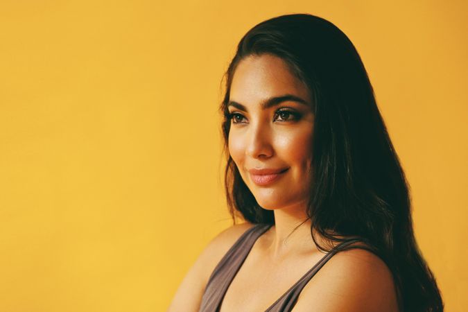 Wistful Hispanic woman looking away from camera in yellow room, copy space