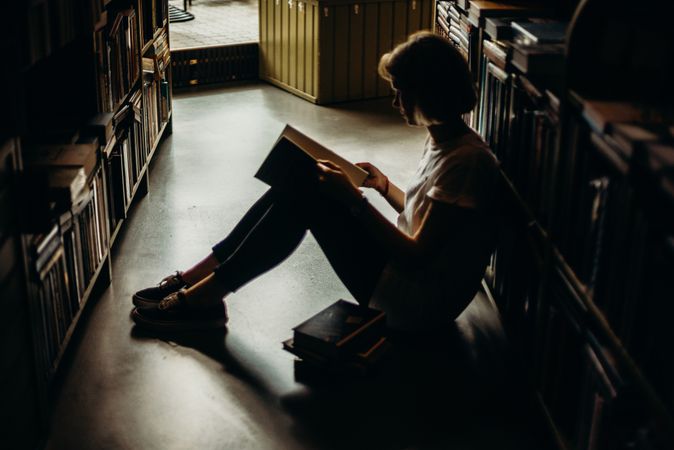 Side view of woman sitting on ground between bookshelves