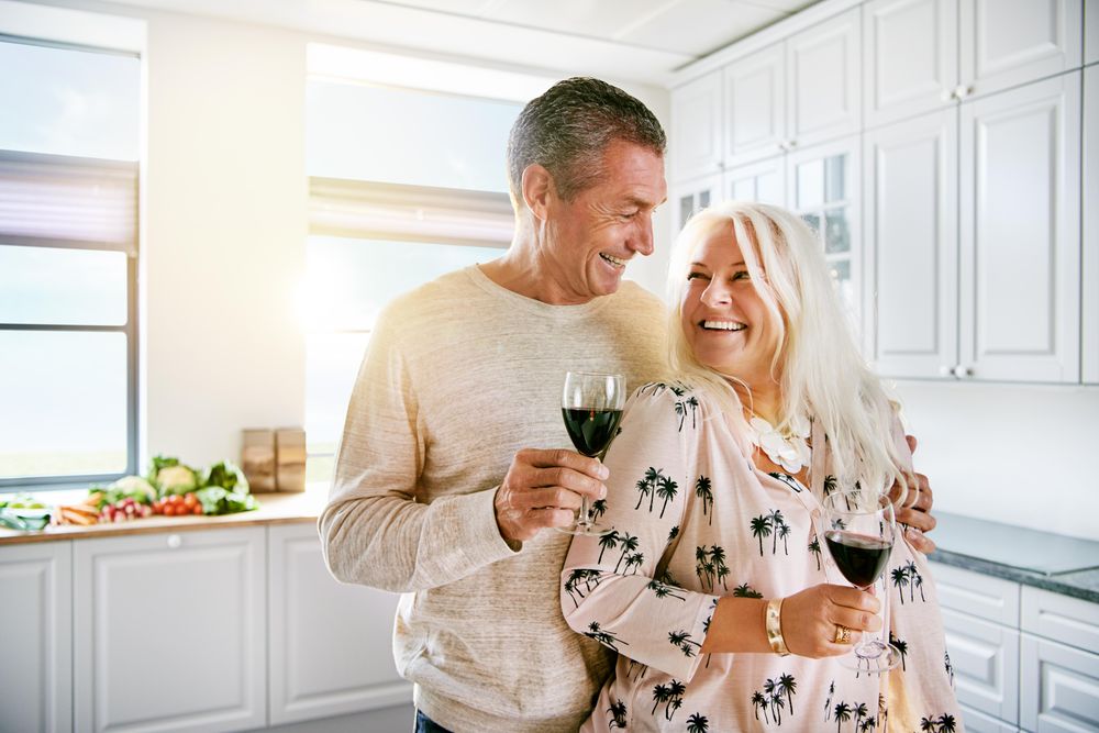 Smiling older couple standing at the kitchen counter with wine