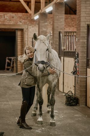 Woman hugging horse with long mane in face in stable