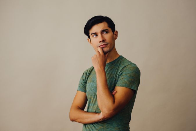 Contemplative Hispanic male holding his chin in neutral room