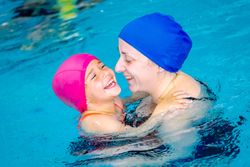 Cheerful girl swimming in pool with mother