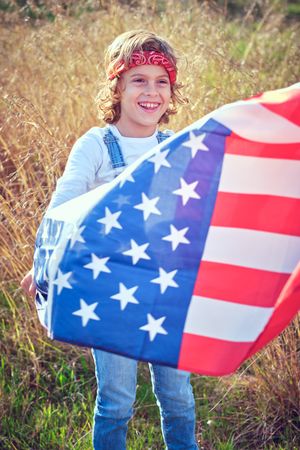 Joyful preteen boy standing in field with waving American flag