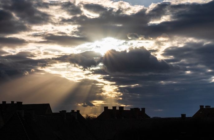 Sunrays peaking through clouds above rooftops