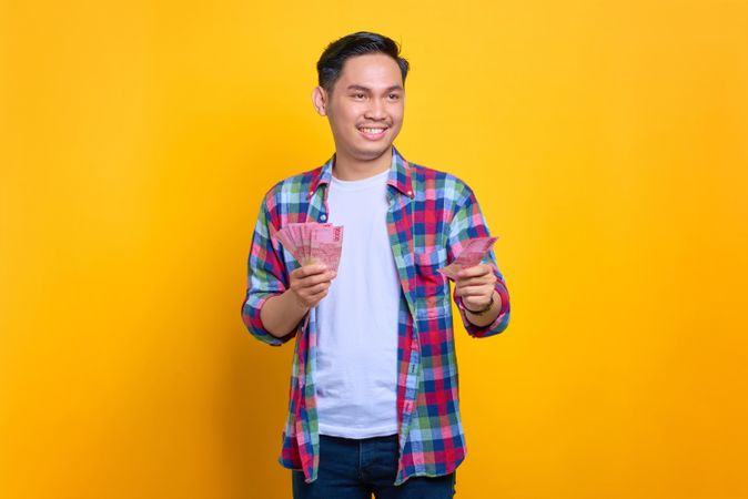 Smiling Asian man holding up cash with both hands in studio shoot