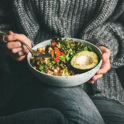 Woman in jeans and sweater eating fresh salad, square crop