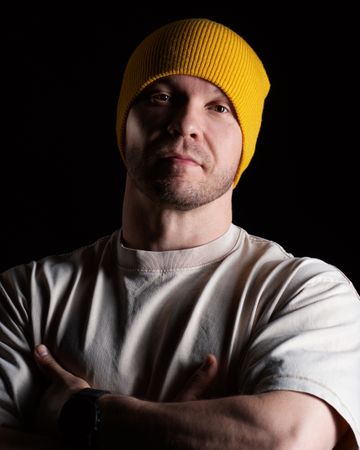 Man in yellow beanie and beige t-shirt, looking confident.