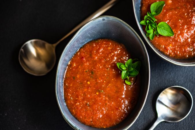 Looking down at tomato soup in bowls with herbs, served with spoon