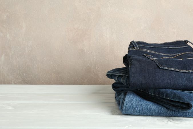 Stack of jeans pants on light background, space for text
